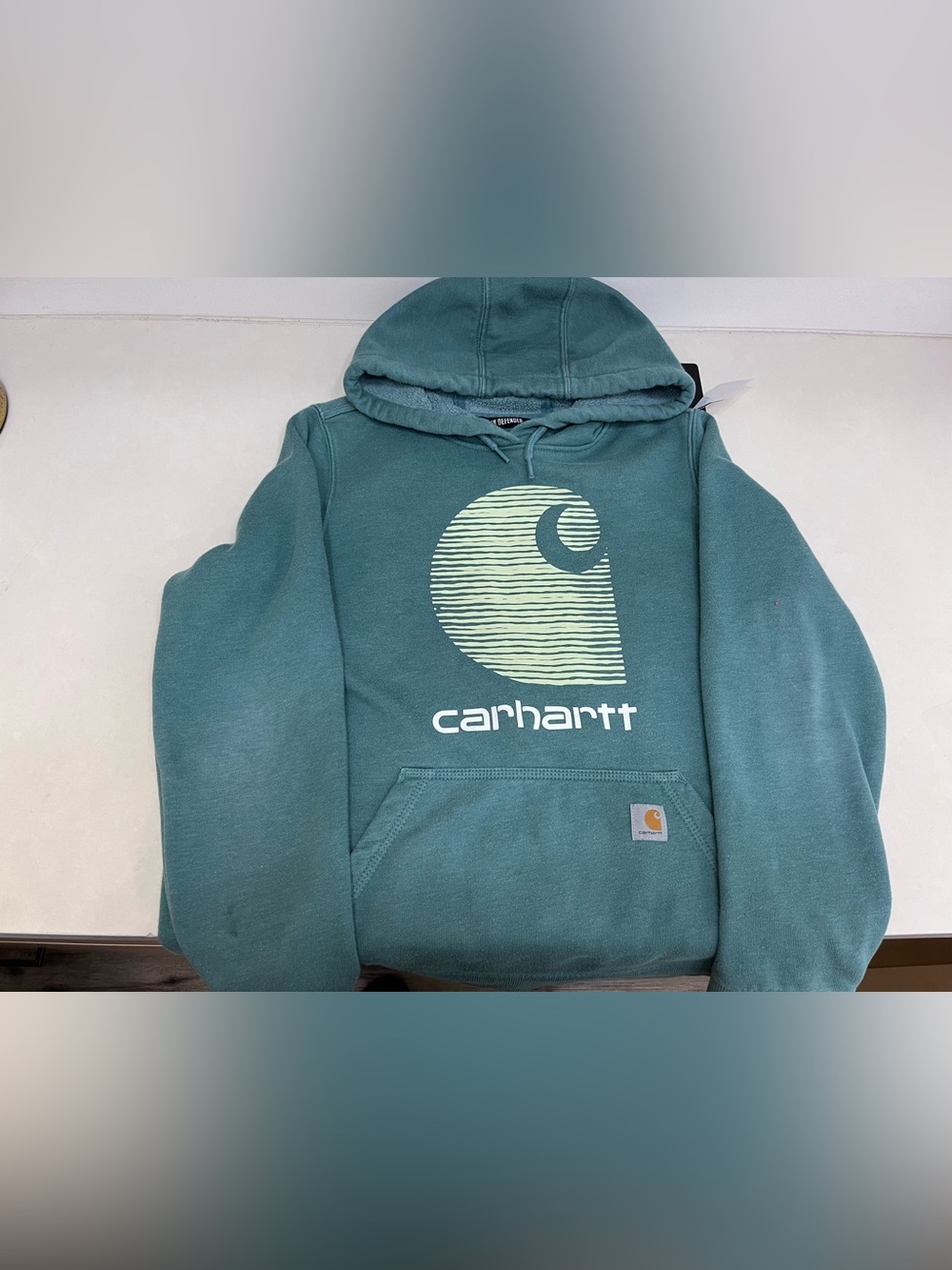 Carhartt teal sweatshirt with orange logo on pink tag